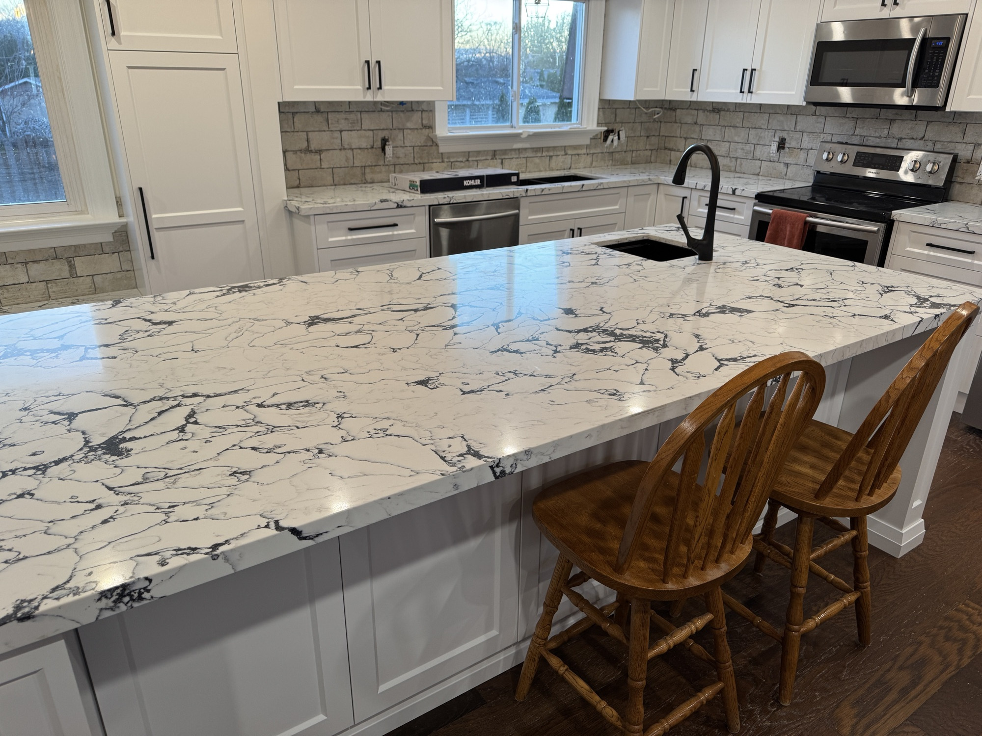 White shaker kitchen with stone subway tile backsplash and a marble island seated with wooden bar stools