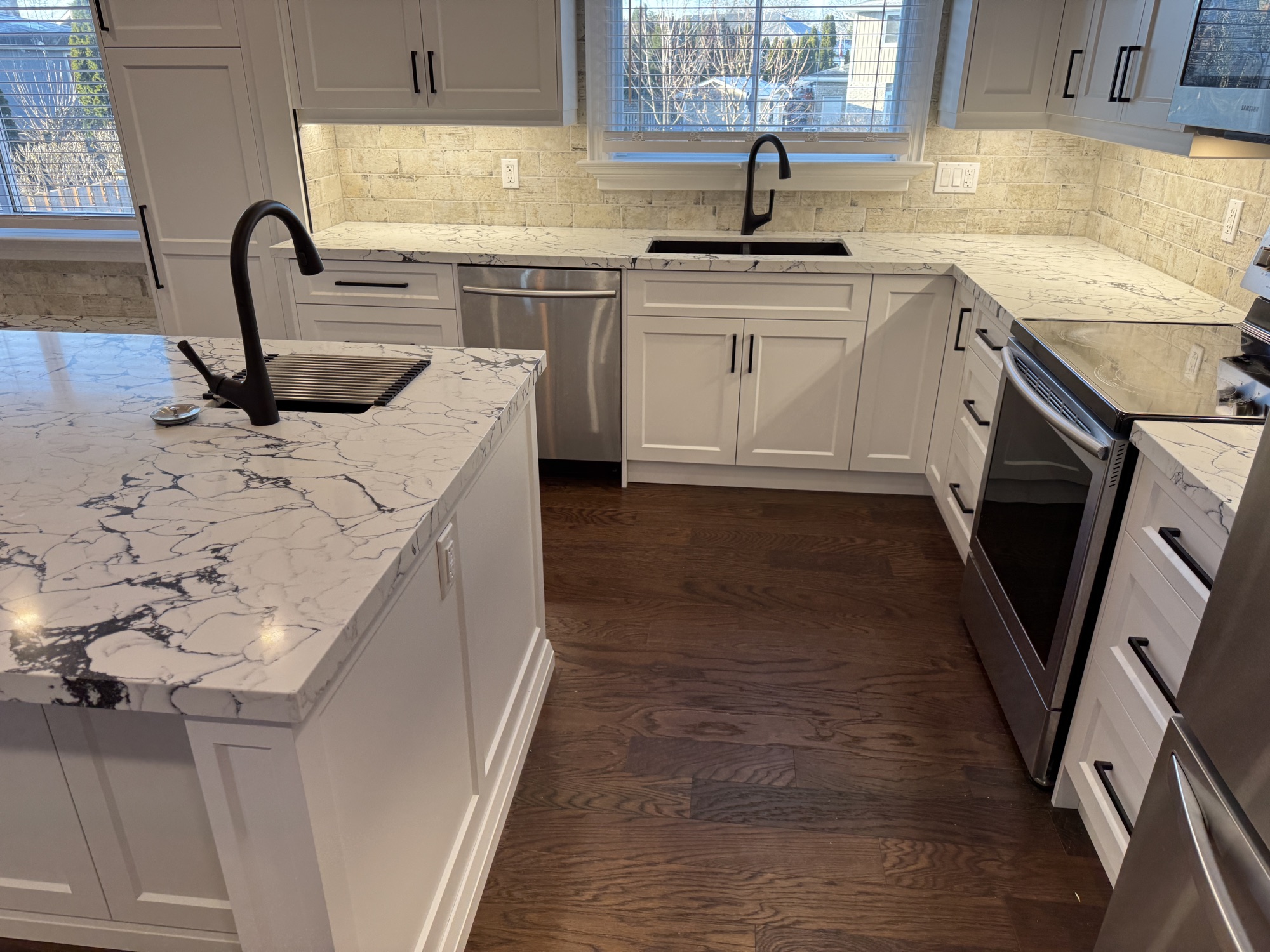 Custom white shaker kitchen with a marble waterfall island, black matte fixtures and dark hardwood flooring in a Niagara Falls renovation