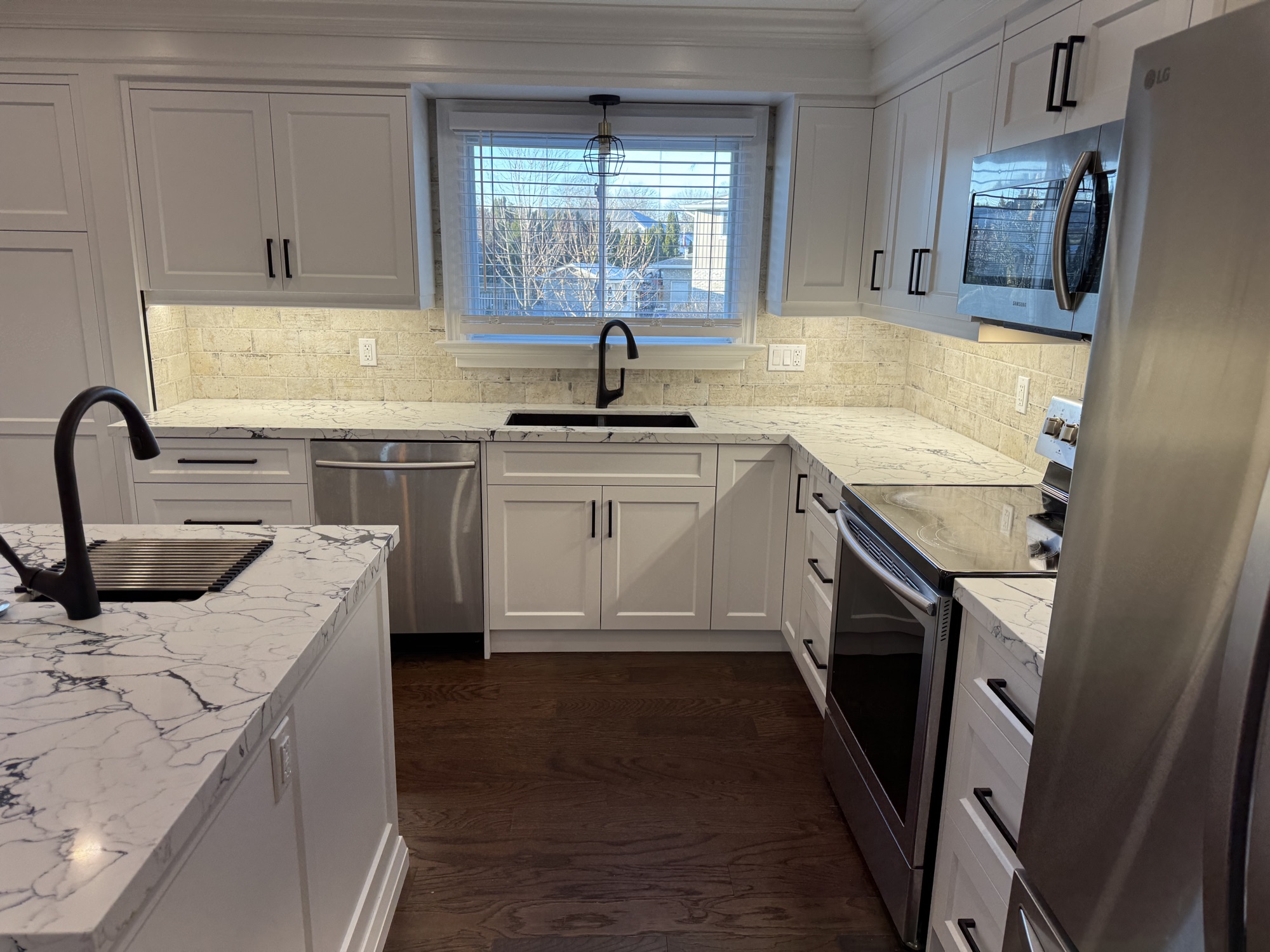 Full run of white cabinetry with a window over the sink and marble countertops in a Niagara kitchen renovation