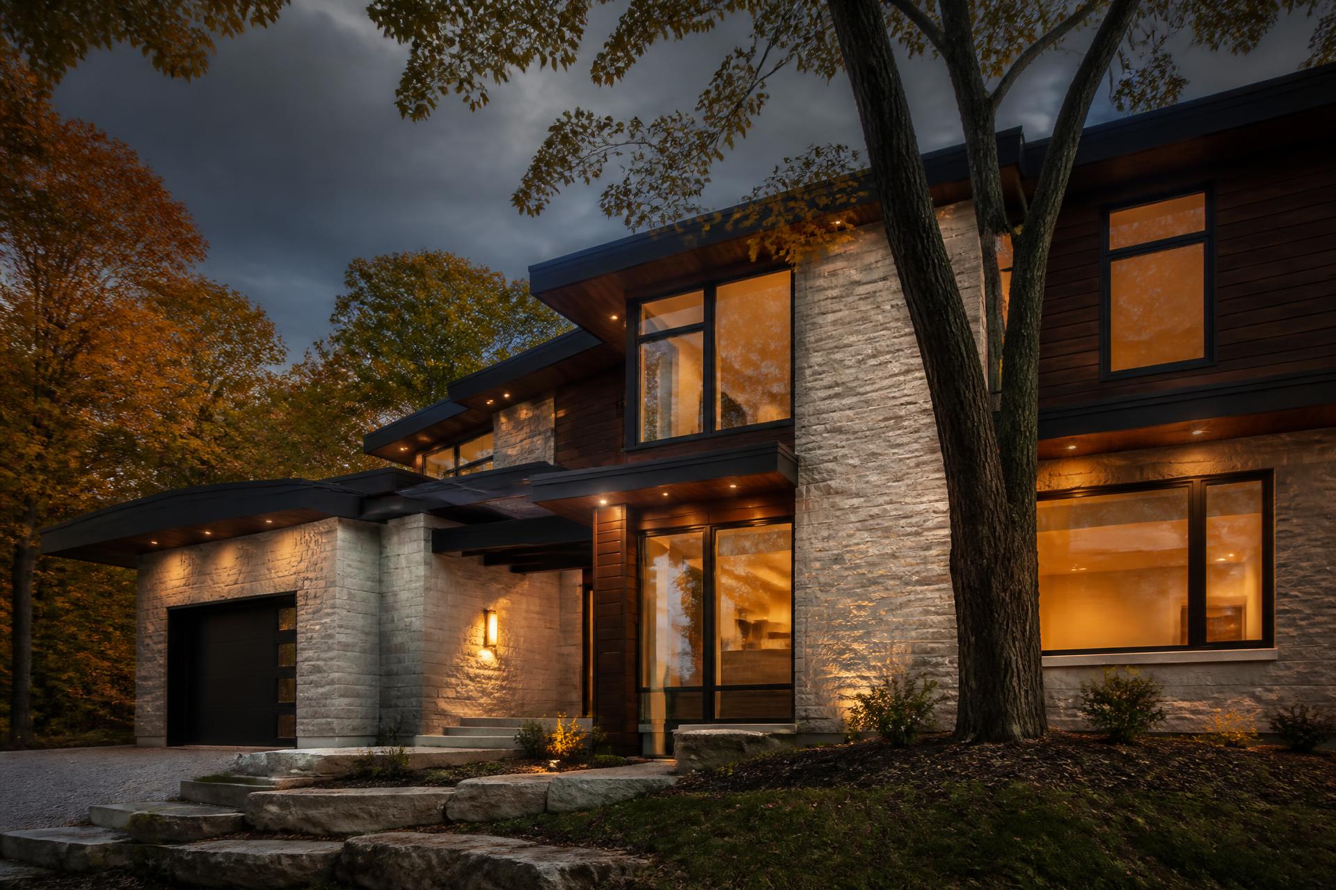 Contemporary home exterior lit at dusk, stone and dark timber cladding